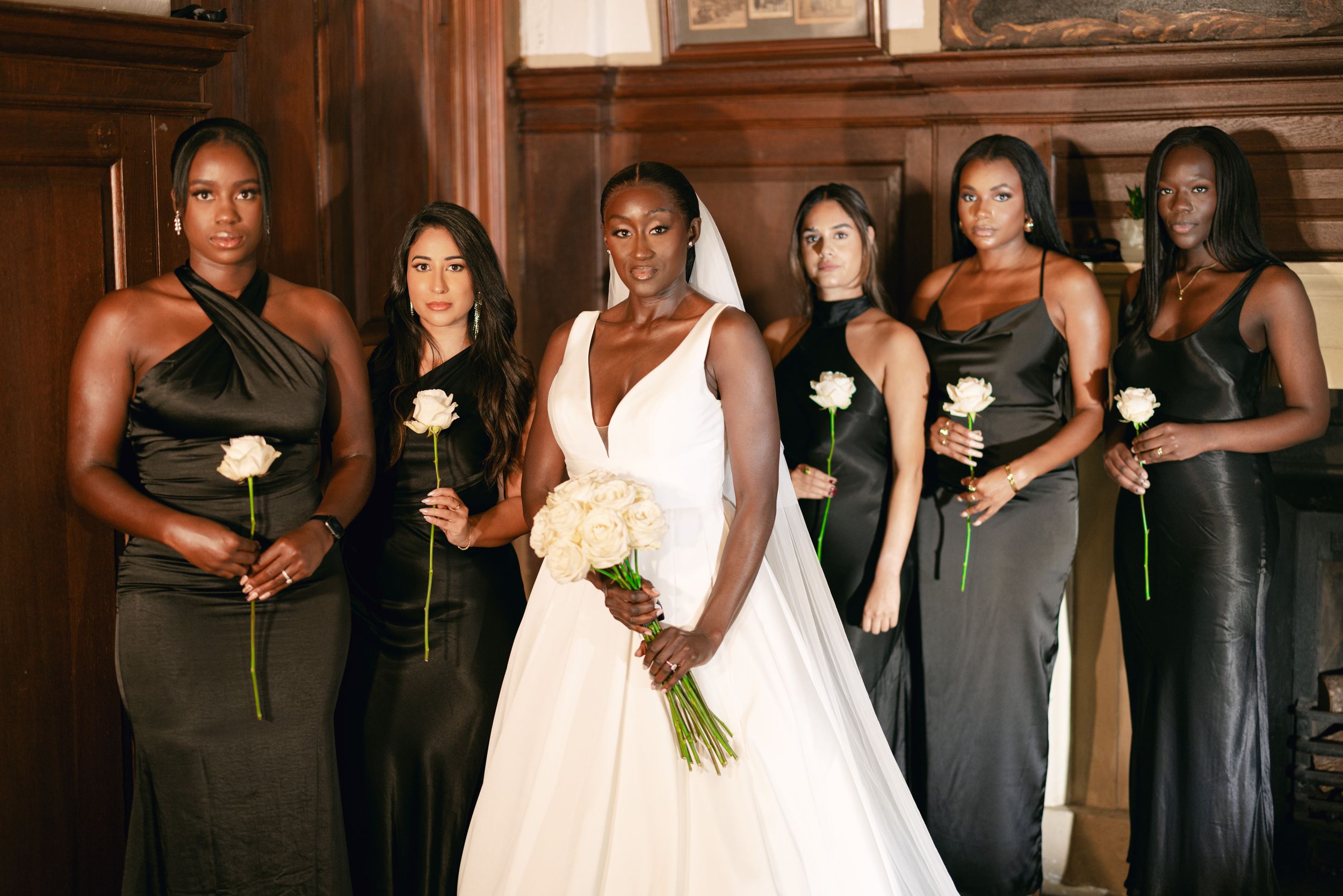 Bridal party wearing elegant black dresses posing with white rose bouquets.