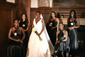 Wedding party portrait featuring bridesmaids in dark gowns holding single stem flowers.