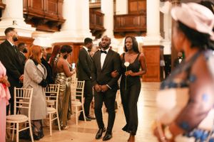 Wedding ceremony guests mingling in an elegant venue with wooden details and white chairs.