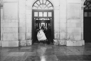 Black and white photo of wedding couple walking through grand archway entrance.