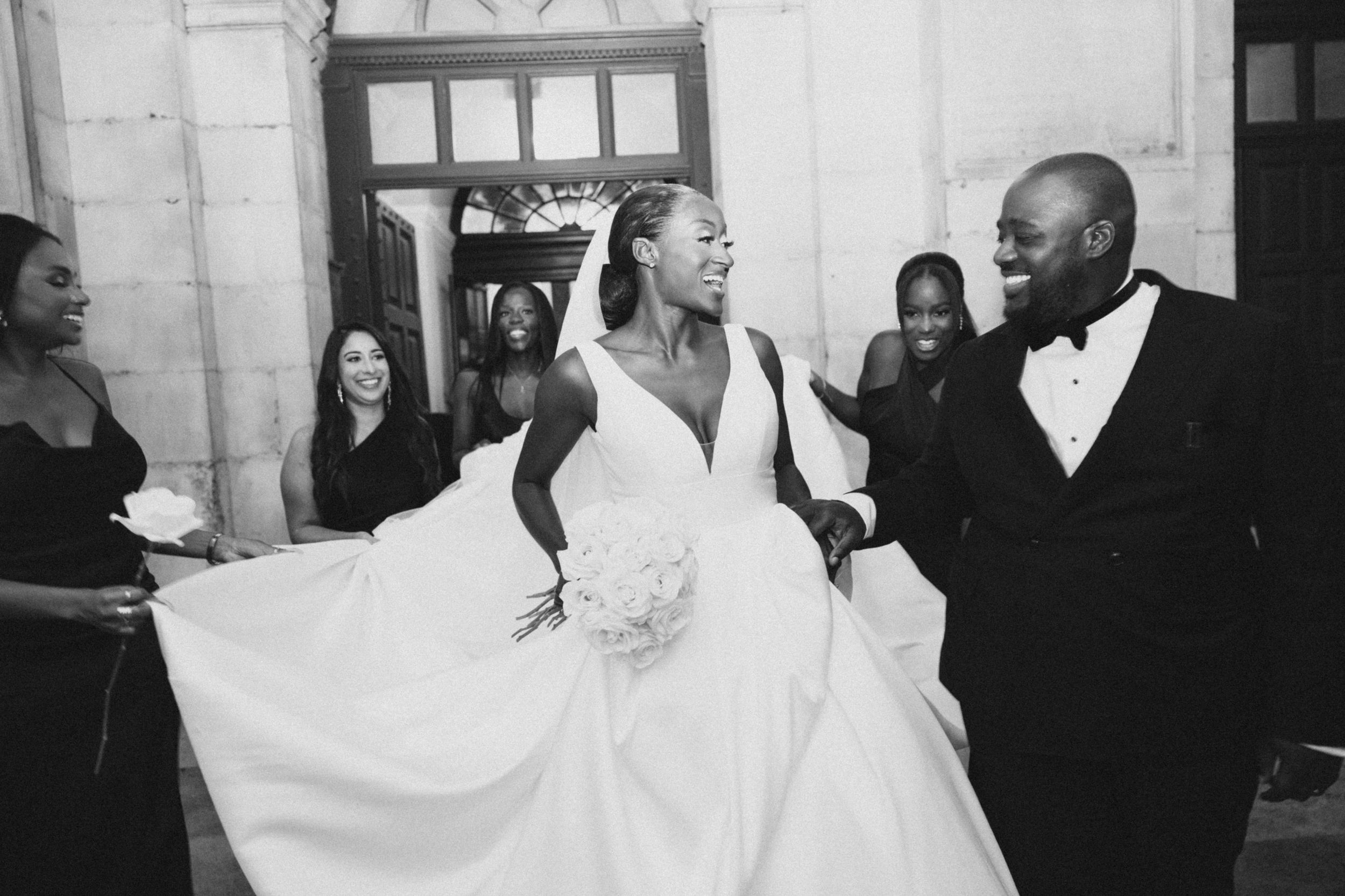 A joyful wedding celebration in black and white showing a bride in a full white gown surrounded by guests.