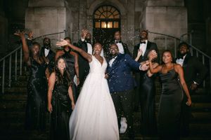 Wedding party strikes fun poses on stone steps during evening celebration.