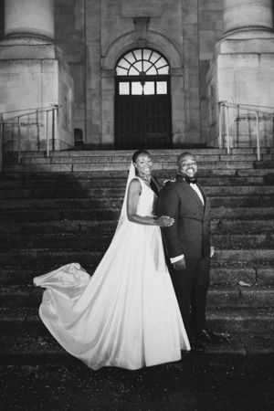 Elegant black and white portrait of newlyweds on historic stone steps with arched doorway.