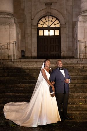 Romantic evening portrait of newlyweds on stone steps with illuminated arched doorway.