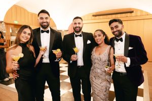 Group of wedding guests in formal attire pose with cocktails during reception.