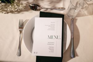 Wedding menu card placed on white plate with silverware on elegant table setting.