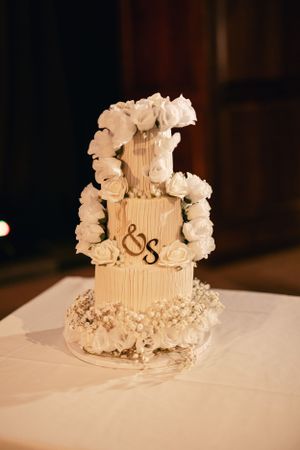 Three-tiered white wedding cake decorated with roses and monogram details.