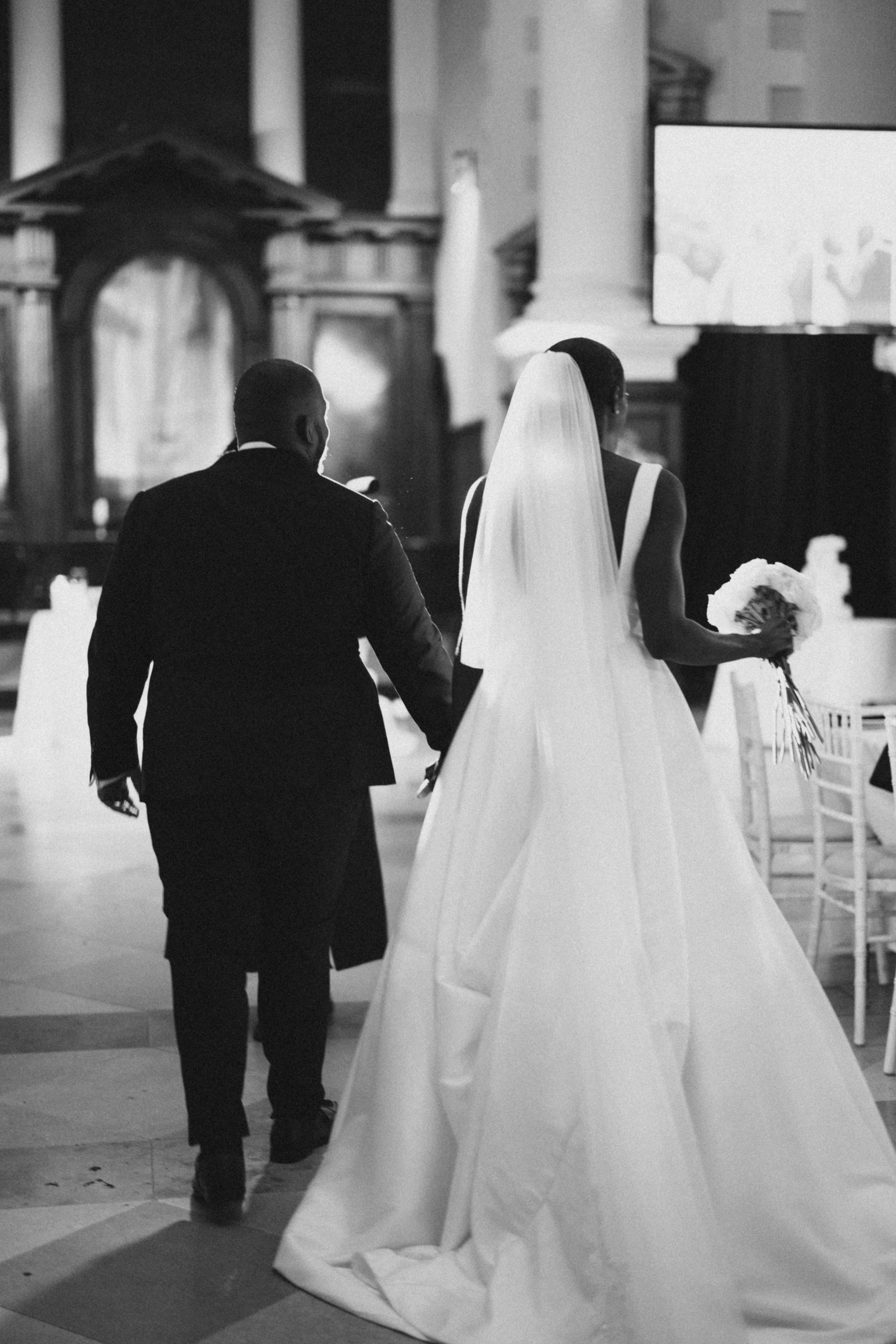 Black and white photo of a couple walking away in elegant wedding attire.