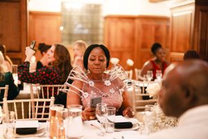 Guests enjoying an elegant wedding reception dinner in a wood-paneled banquet hall with white chiavari chairs.