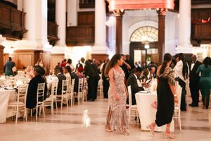 Guests mingling at an elegant wedding reception in a grand hall with white columns and chairs.