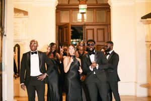 Wedding party dressed in formal black attire posing together in an elegant hallway.