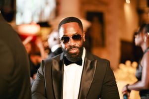 Stylish guest in a black tuxedo and sunglasses at a formal wedding reception.