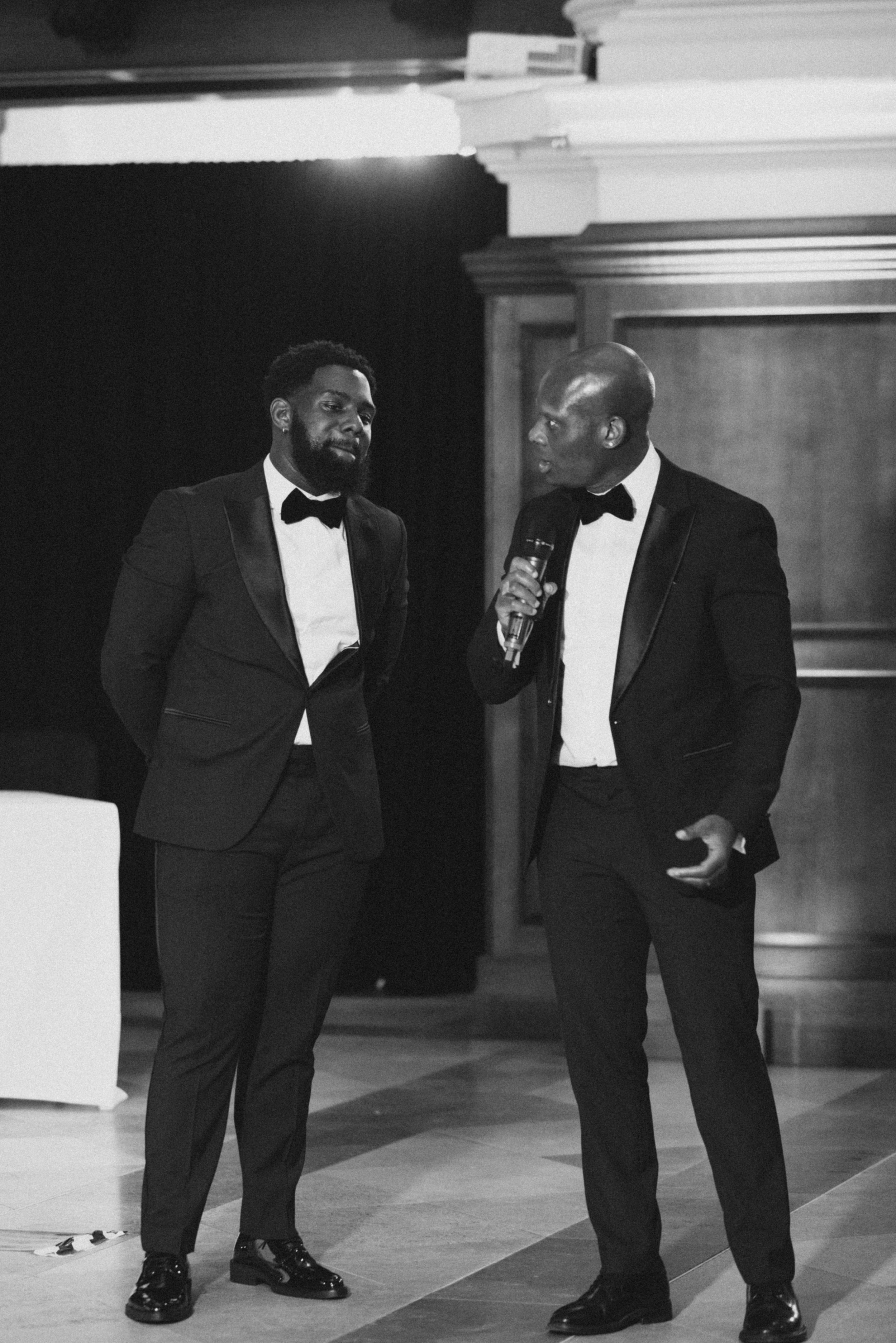 Two men in tuxedos sharing a conversation during formal black-tie event.