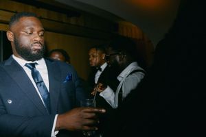 Stylishly dressed guest in dark suit holds drink at formal event.