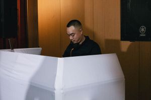 Person in black attire looking down at white surface in dimly lit room.