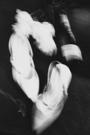 Artistic black and white photo of wedding shoes and champagne bottle.