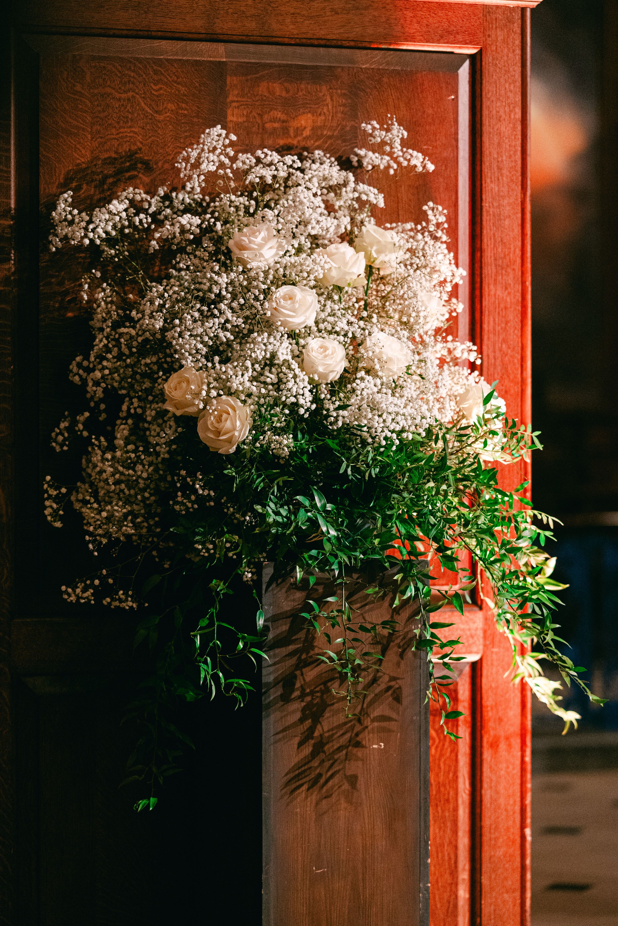 Romantic white rose and baby's breath floral arrangement against a wooden backdrop.