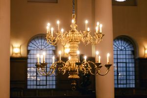 A vintage brass chandelier with glowing candles hangs in an arched window setting.
