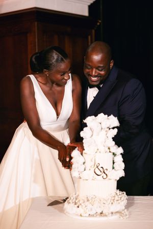 A couple cuts into their elegant white wedding cake decorated with floral details.