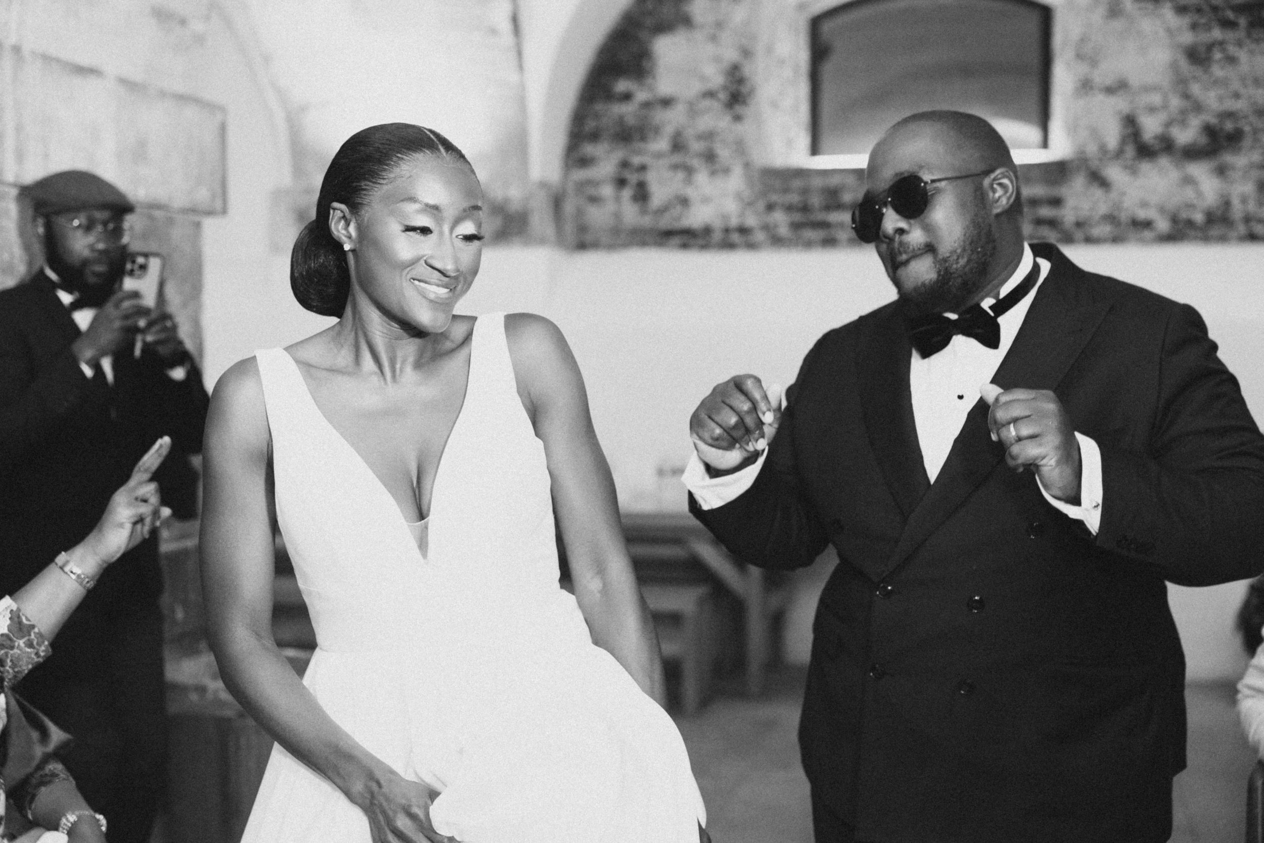A couple in formal attire dances together at a wedding reception in black and white.