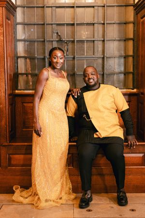 Wedding guests pose together in formal attire against wooden paneled wall.
