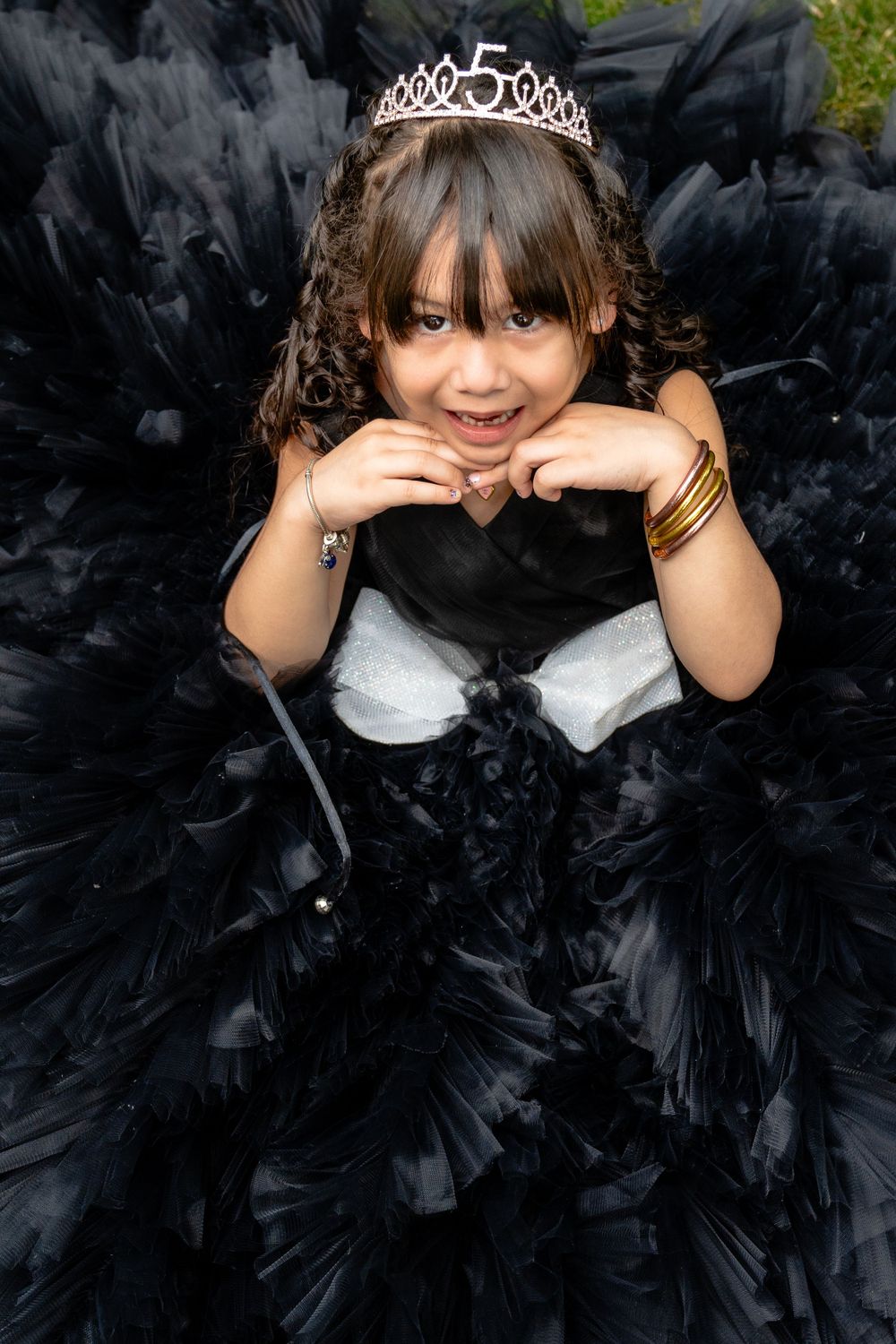 A young child in a black tulle dress and tiara poses playfully for a portrait.