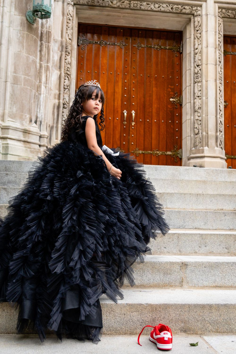 Dramatic black tulle ball gown photographed on stone steps in front of ornate wooden doors.