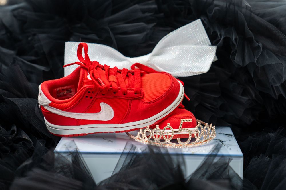 Red Nike sneaker with white swoosh logo displayed with a tiara against black background.