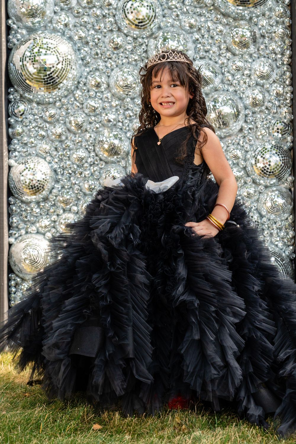 Black ruffled ball gown against silver disco ball backdrop creates glamorous scene.