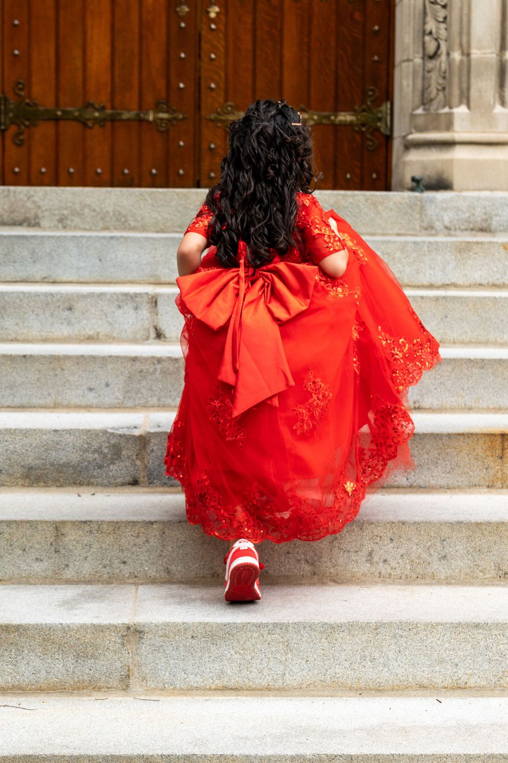 Red lace dress with large bow detail photographed from behind on stone steps.