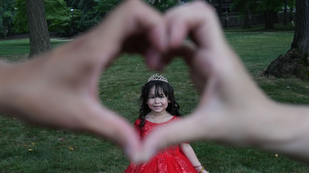 A creative photo showing a child in red dress framed by hands forming a heart shape.