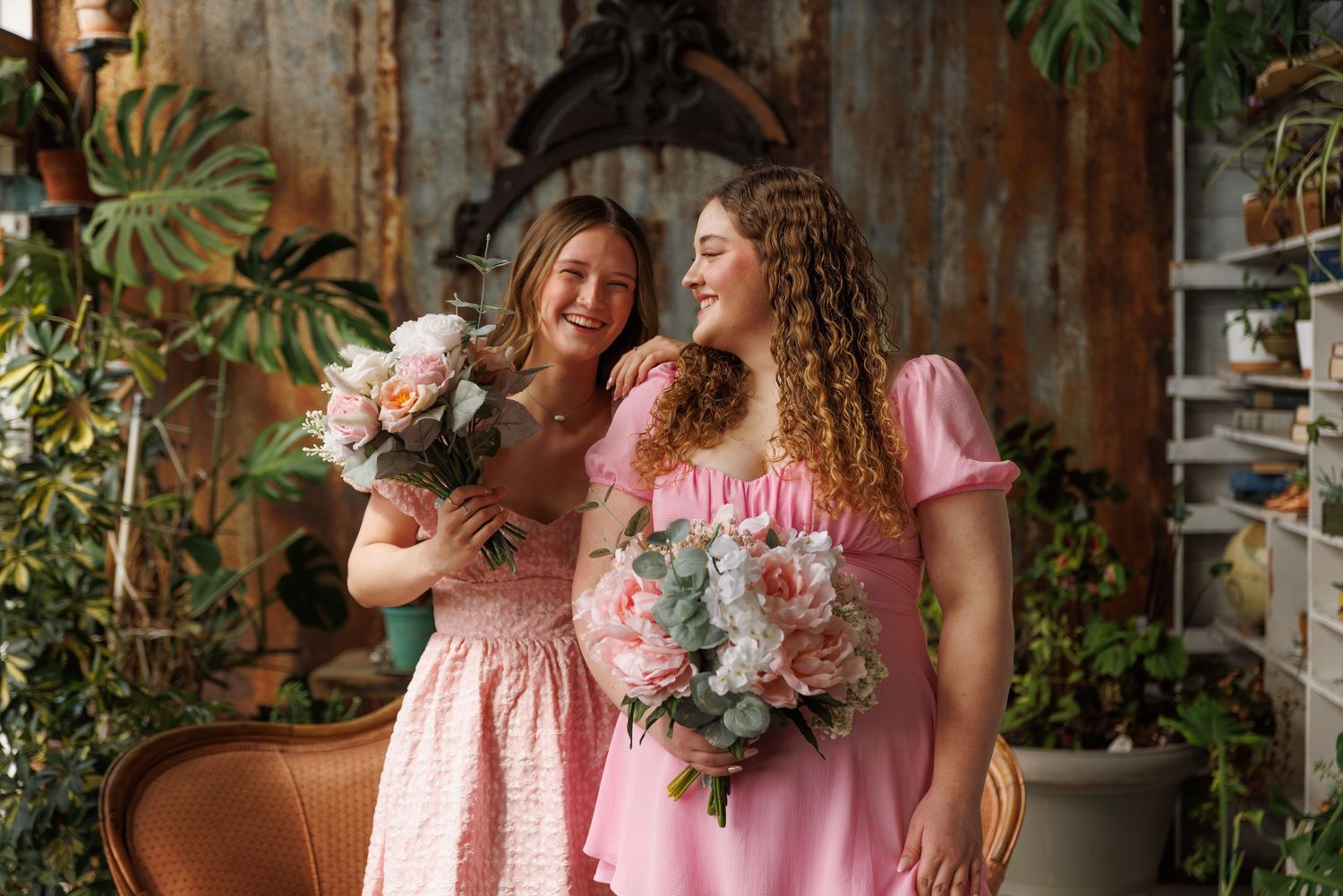 high school best friends laugh while photographed together holding bouquets of flowers.