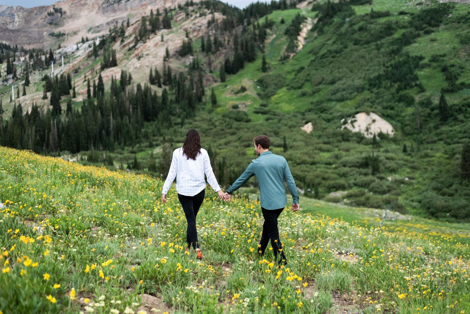 People hiking through a vibrant alpine meadow filled with yellow wildflowers in the mountains during summer.
