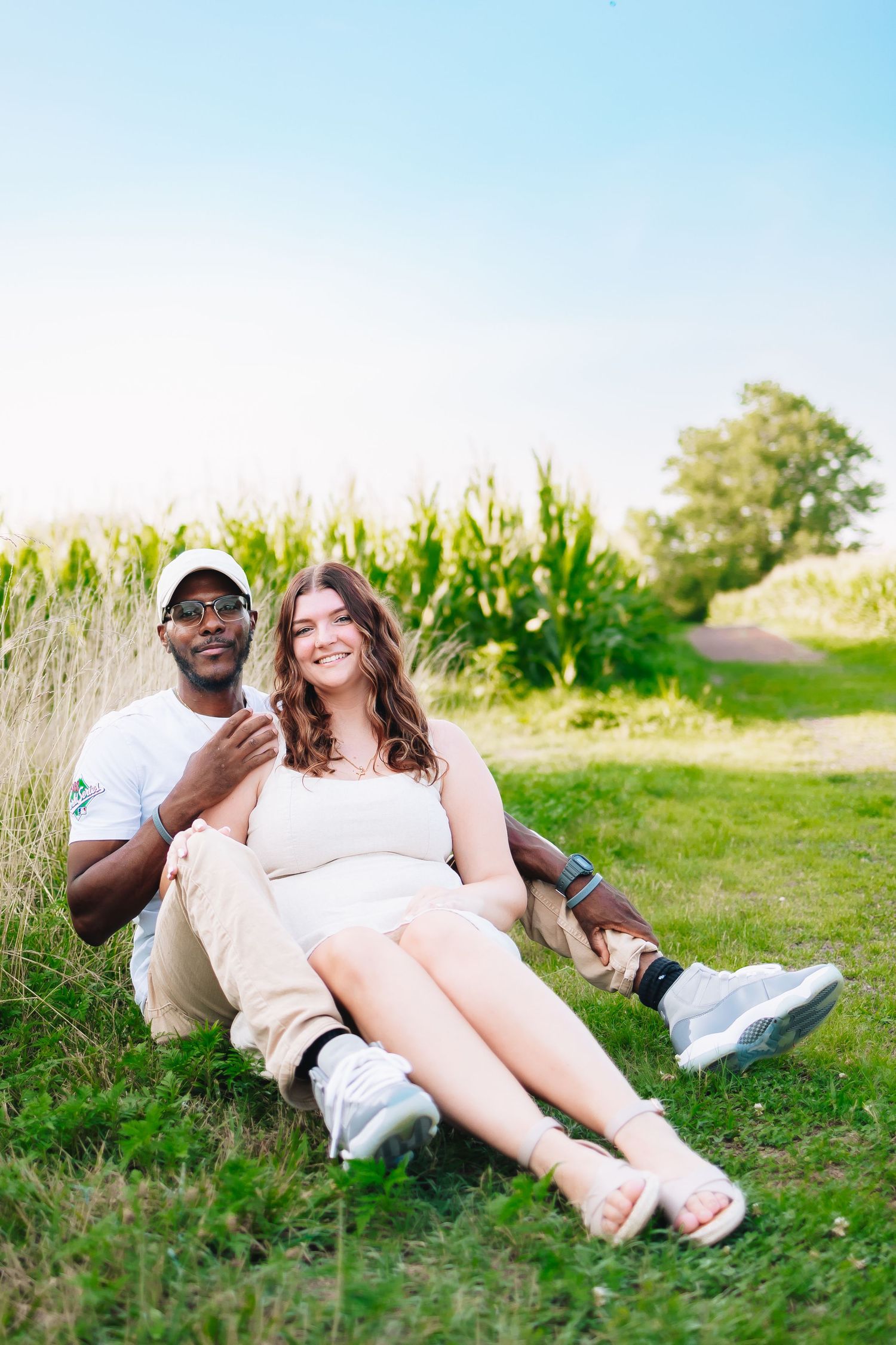 A couple relaxing together on grass near a cornfield on a bright summer day.