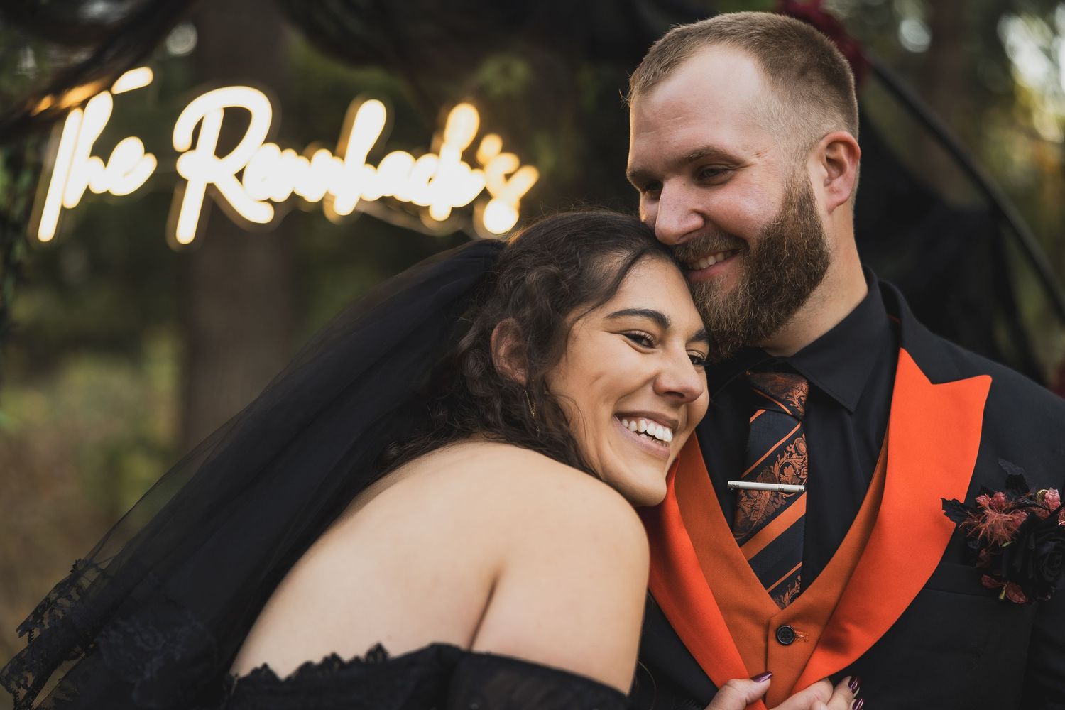 A couple shares a joyful moment together outdoors during in their backyard Halloween wedding photoshoot, wearing orange and black attire.