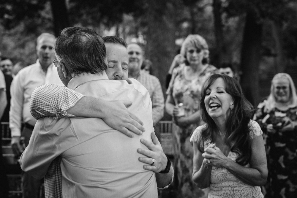 Joyful wedding guests embrace and laugh during an outdoor celebration.