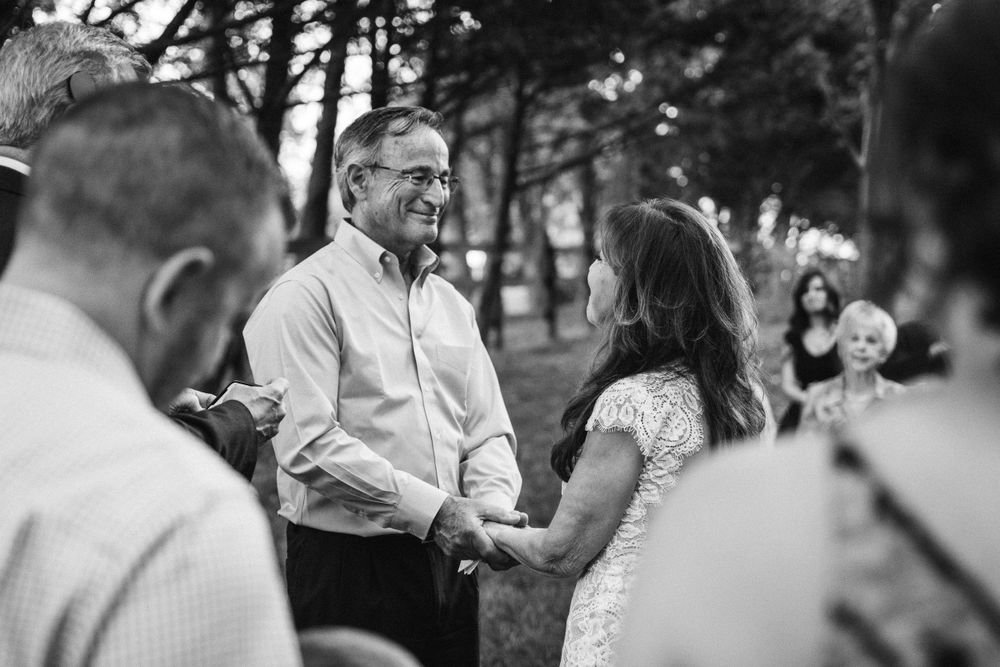 A black and white ceremony capture showing a couple exchanging vows surrounded by guests.
