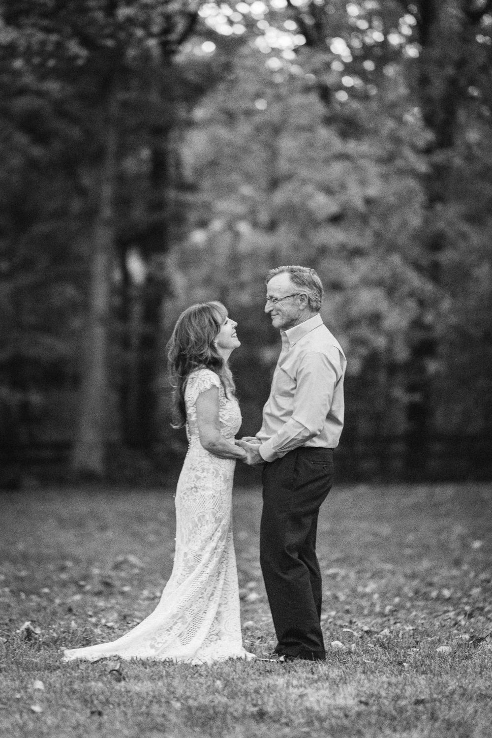 A black and white wedding portrait of a couple holding hands in a wooded setting.
