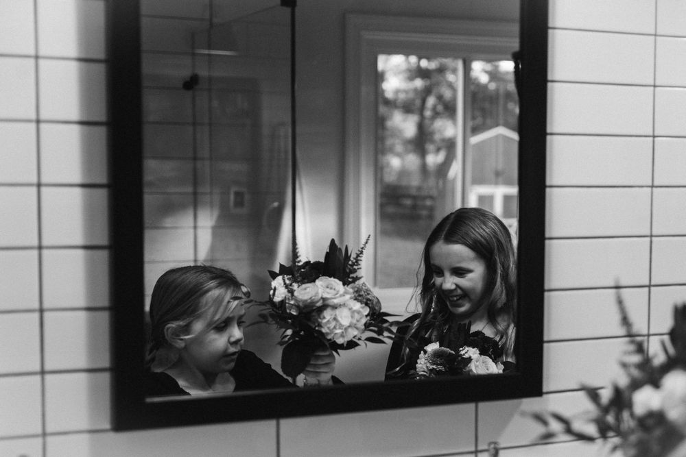A black and white reflection in a mirror shows two people arranging flowers together.
