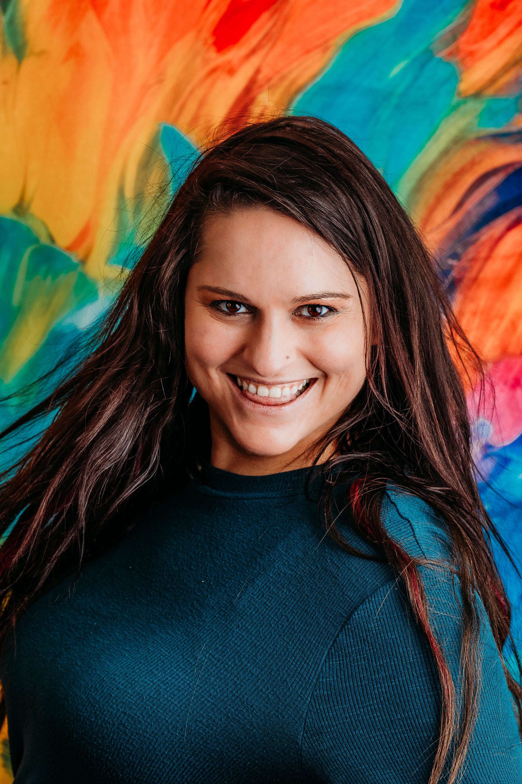 Emina Delic wearing a blue sweater against a vibrant painted background. Boudoir Photographer is West Michigan. www.minasphoto.com