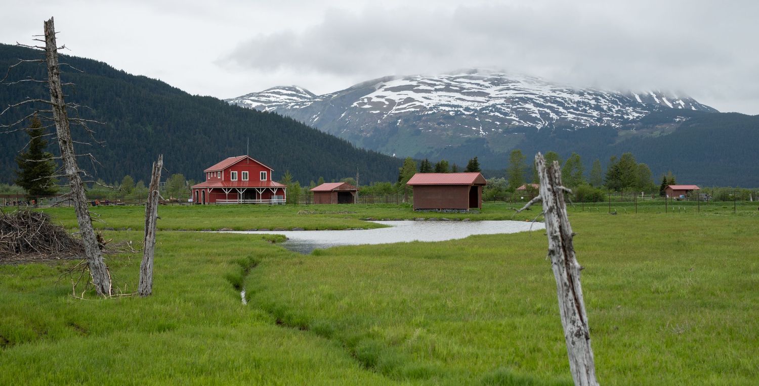 Panoramic mountain landscape with red cabin and snow-capped peaks in the distance.