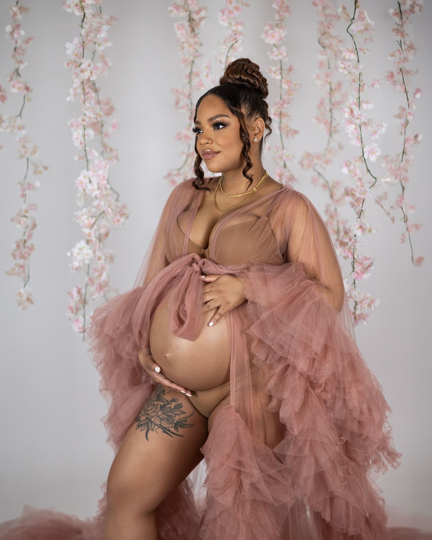 A maternity photo featuring someone in a flowing dusty rose tulle robe against a floral backdrop with cherry blossoms.