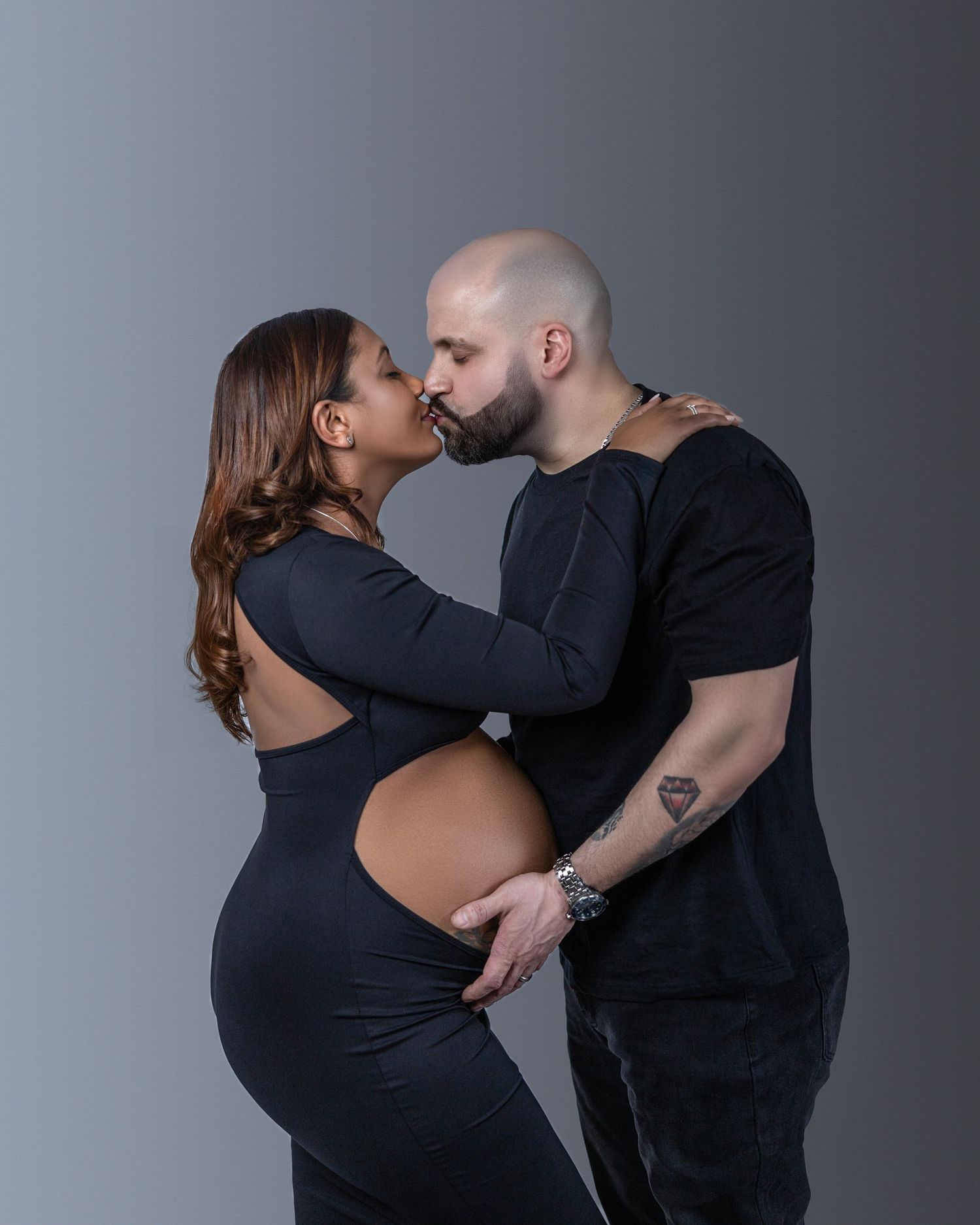 A touching maternity photo shows an intimate moment between a couple against a gray background.