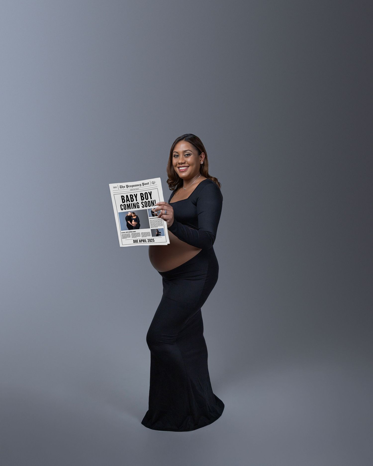 Person in a black formal dress poses against gray backdrop while holding a newspaper.