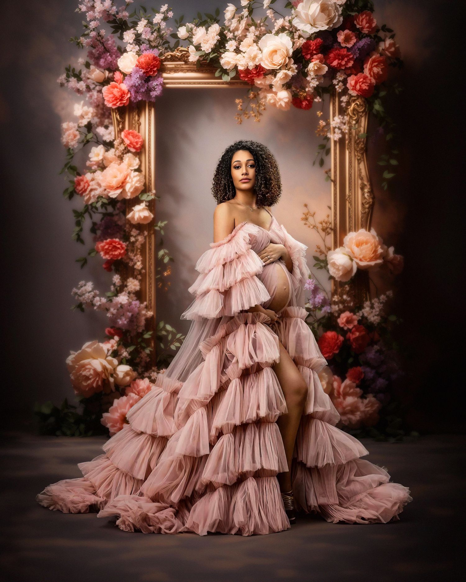 Romantic portrait in blush pink ruffled gown surrounded by floral arch with roses and soft lighting.