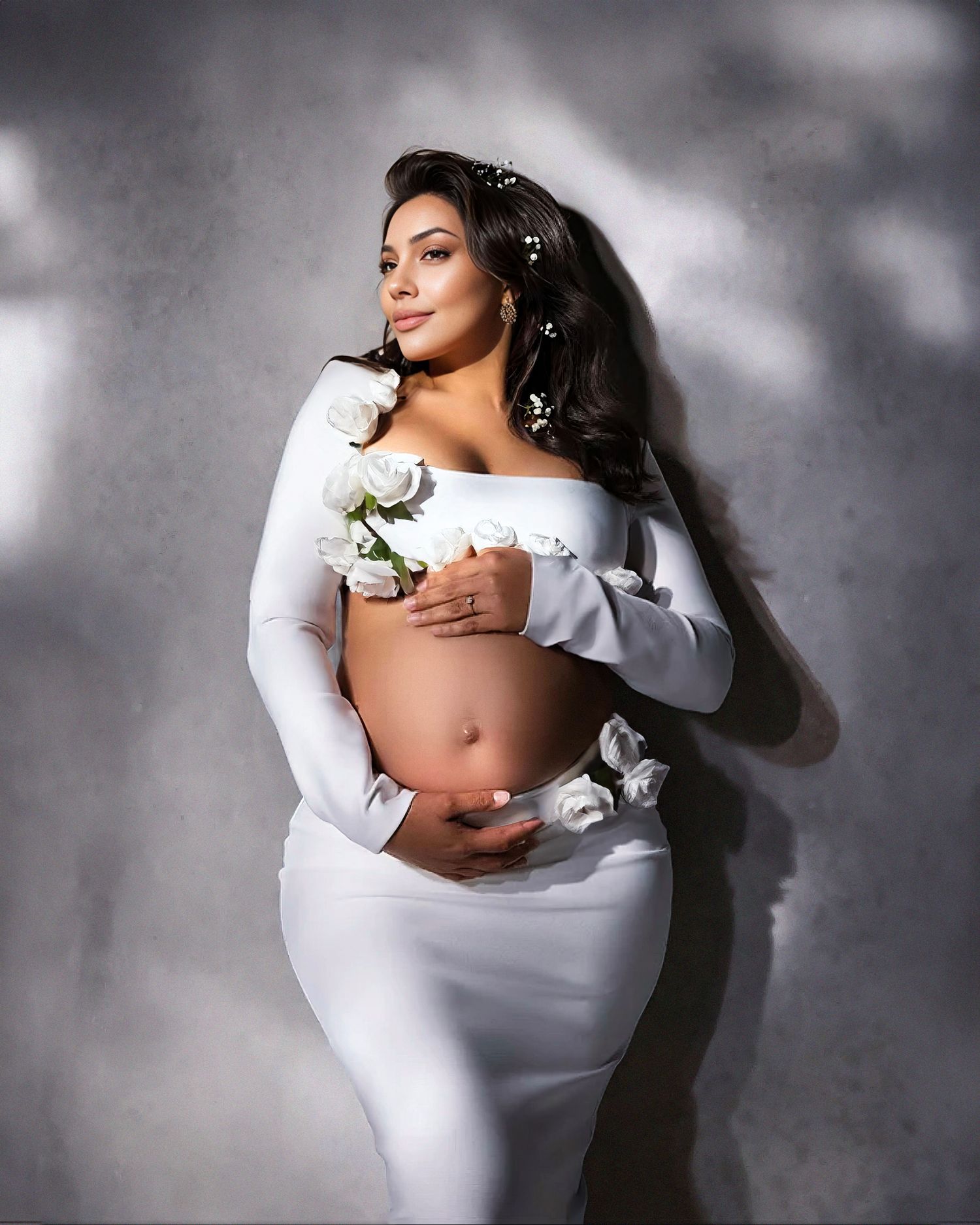 A maternity photo featuring a figure in white clothing with flowing fabric and delicate white flowers against a moody backdrop.
