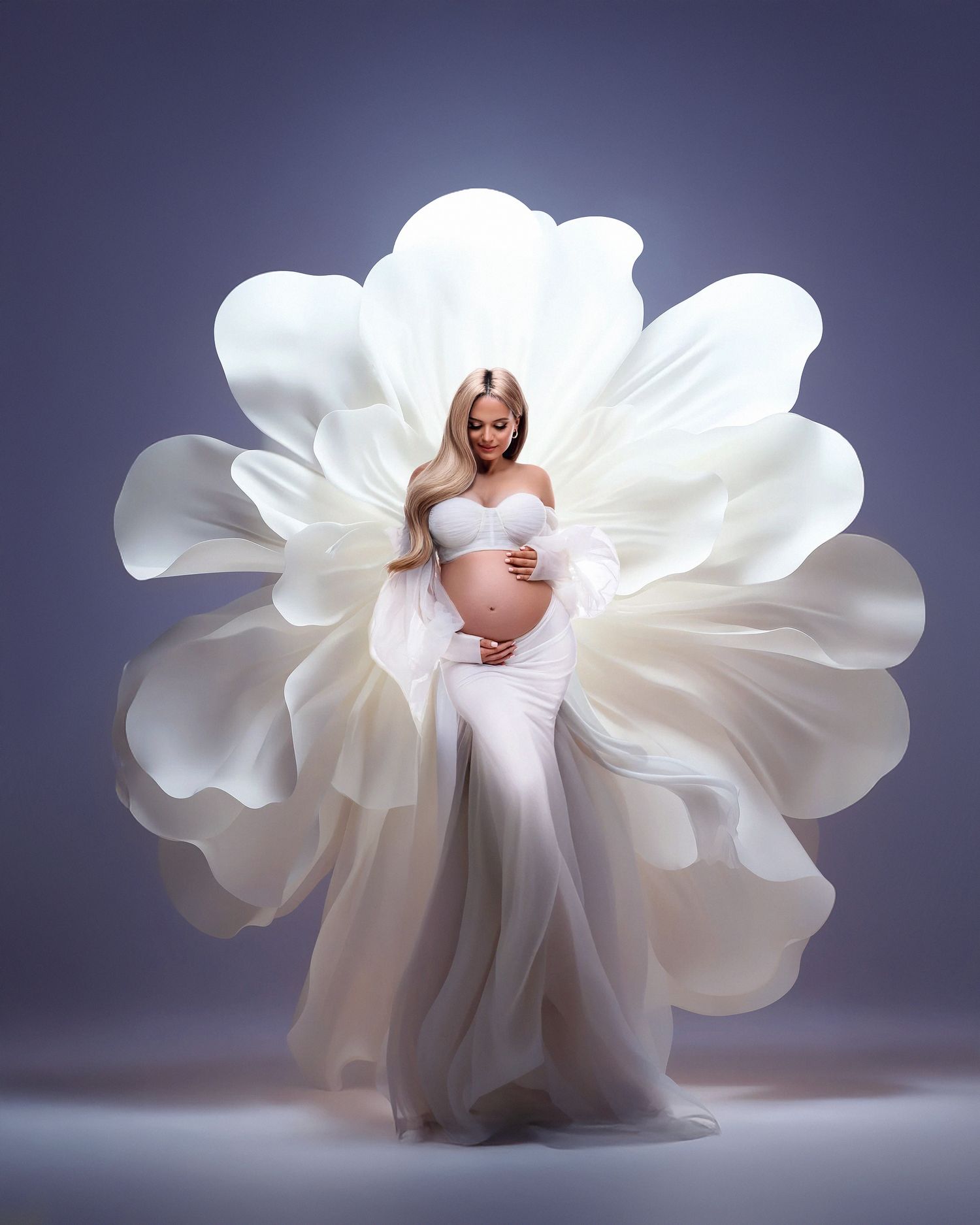 Artistic maternity portrait with flowing white fabric petals creating a dramatic flower-like backdrop against a dark background.