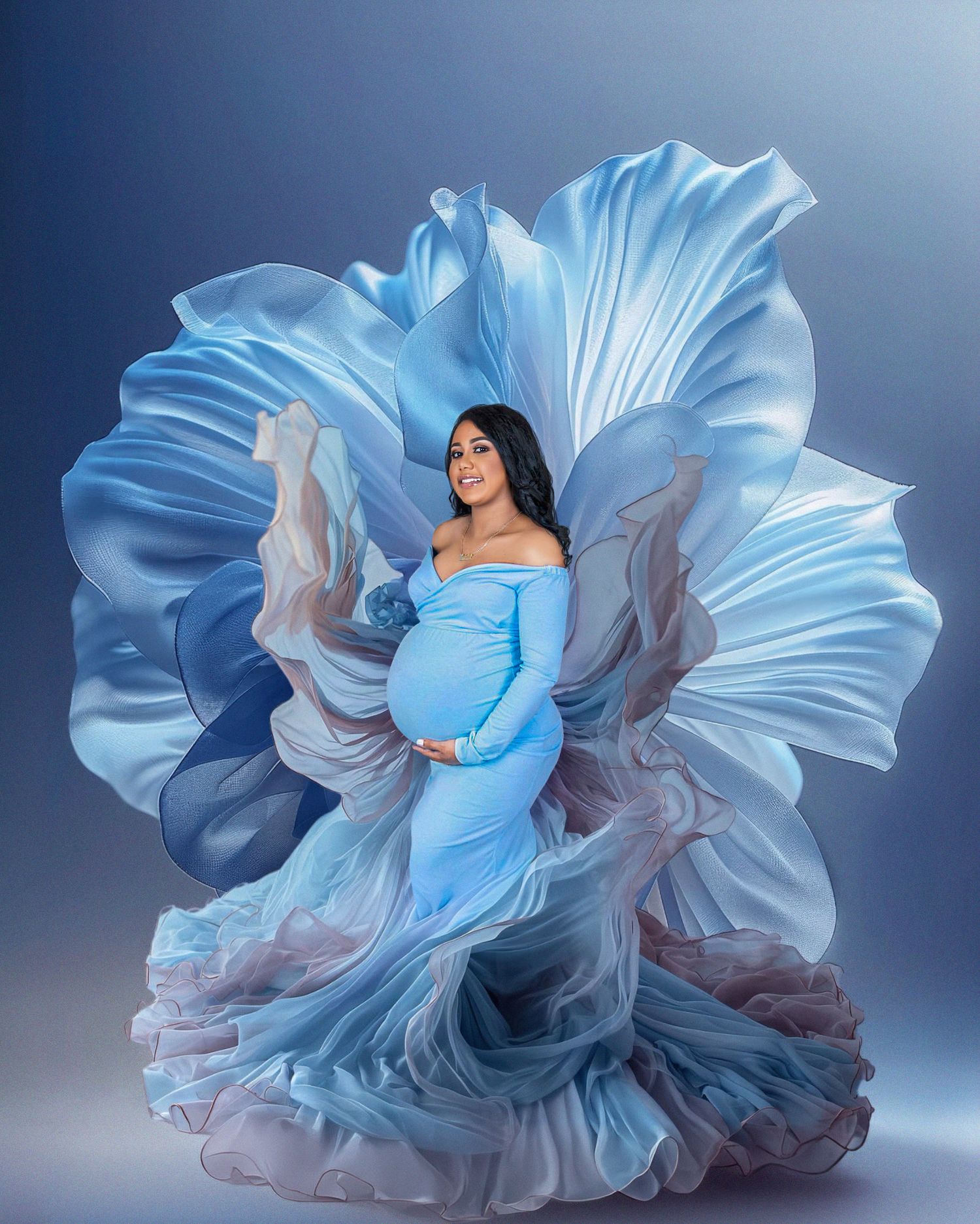 Elegant maternity portrait featuring a flowing light blue gown with dramatic ruffles against a dark blue background.