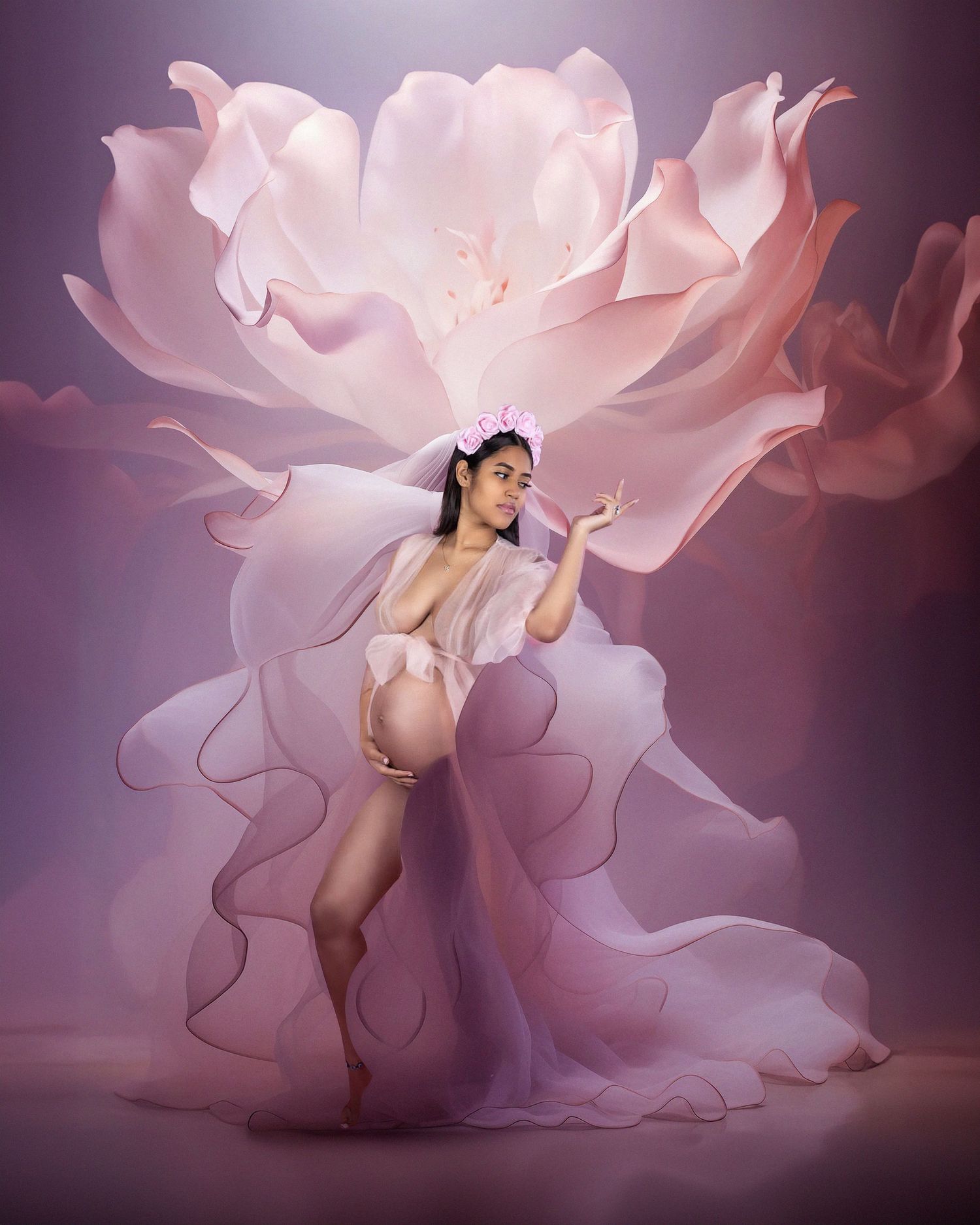 Artistic maternity photo with flowing pink fabric creating a rose-like backdrop in ethereal lighting.