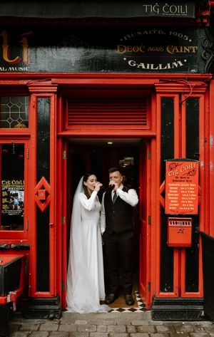 A wedding couple poses outside a red-painted Irish pub storefront.